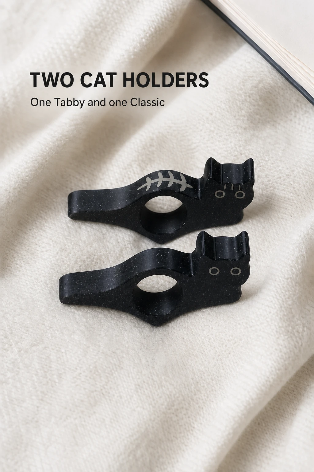 Two black cat holders on light fabric beside a book.