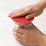 A hand places a silicone gripper pad over a jar lid before turning it.