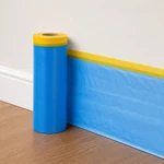 Film azul con cinta amarilla extendido junto a un rodapié blanco sobre un suelo de madera.