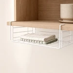 White under-shelf basket holding folded kitchen cloths beneath a wooden shelf
