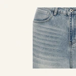 Nahaufnahme von hellblauem Denim an Bund und Vordertasche mit Gürtelschlaufen, Metallknopf und diagonaler Webstruktur.