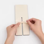 Hands tying an example ribbon around one slotted wooden board; ribbon not included